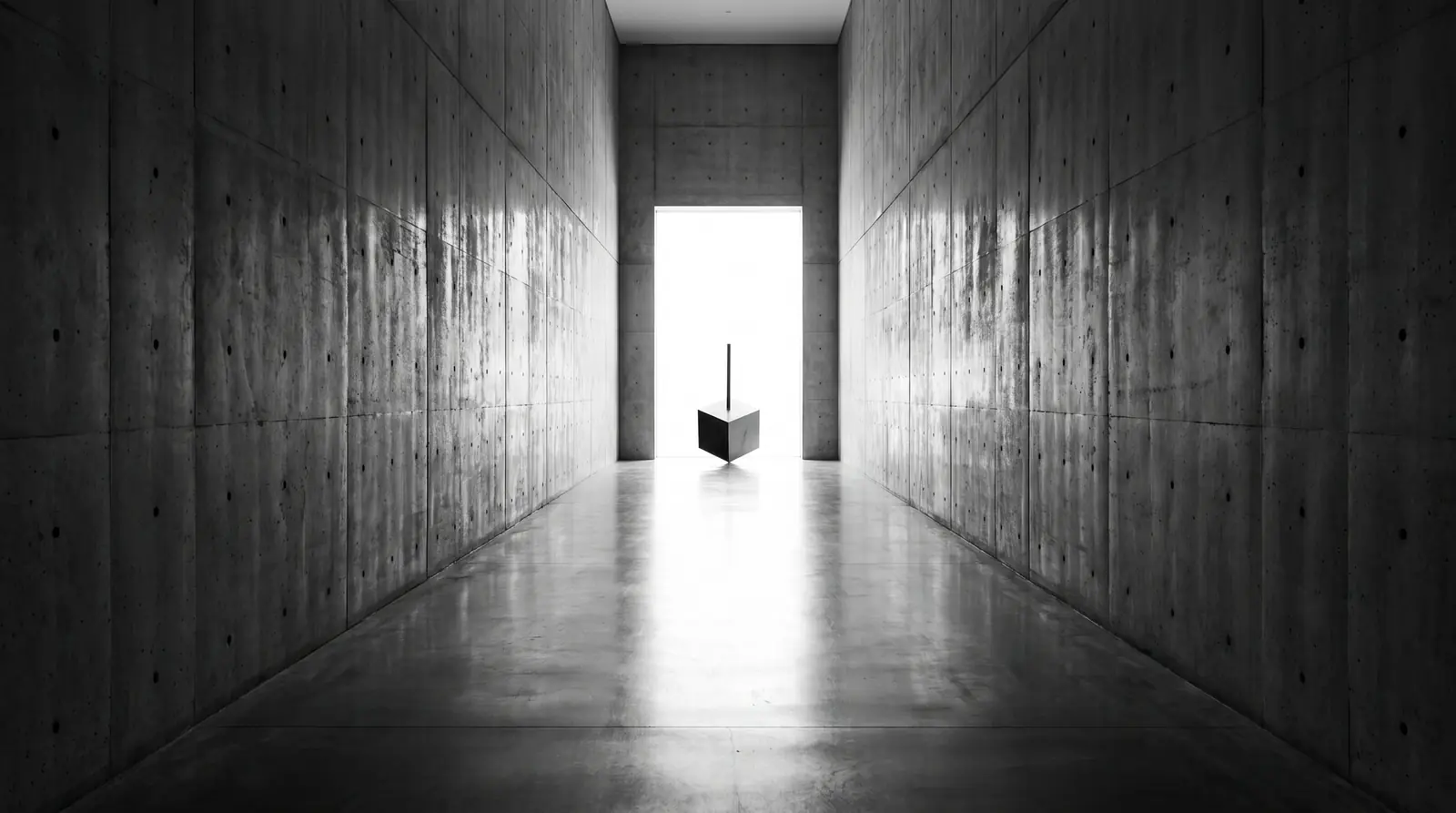 Corredor de concreto que termina numa abertura de luz, com o cubo na soleira